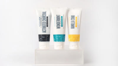 Three Schmidt's toothpastes standing vertically on clear frosted lucite platform with white background